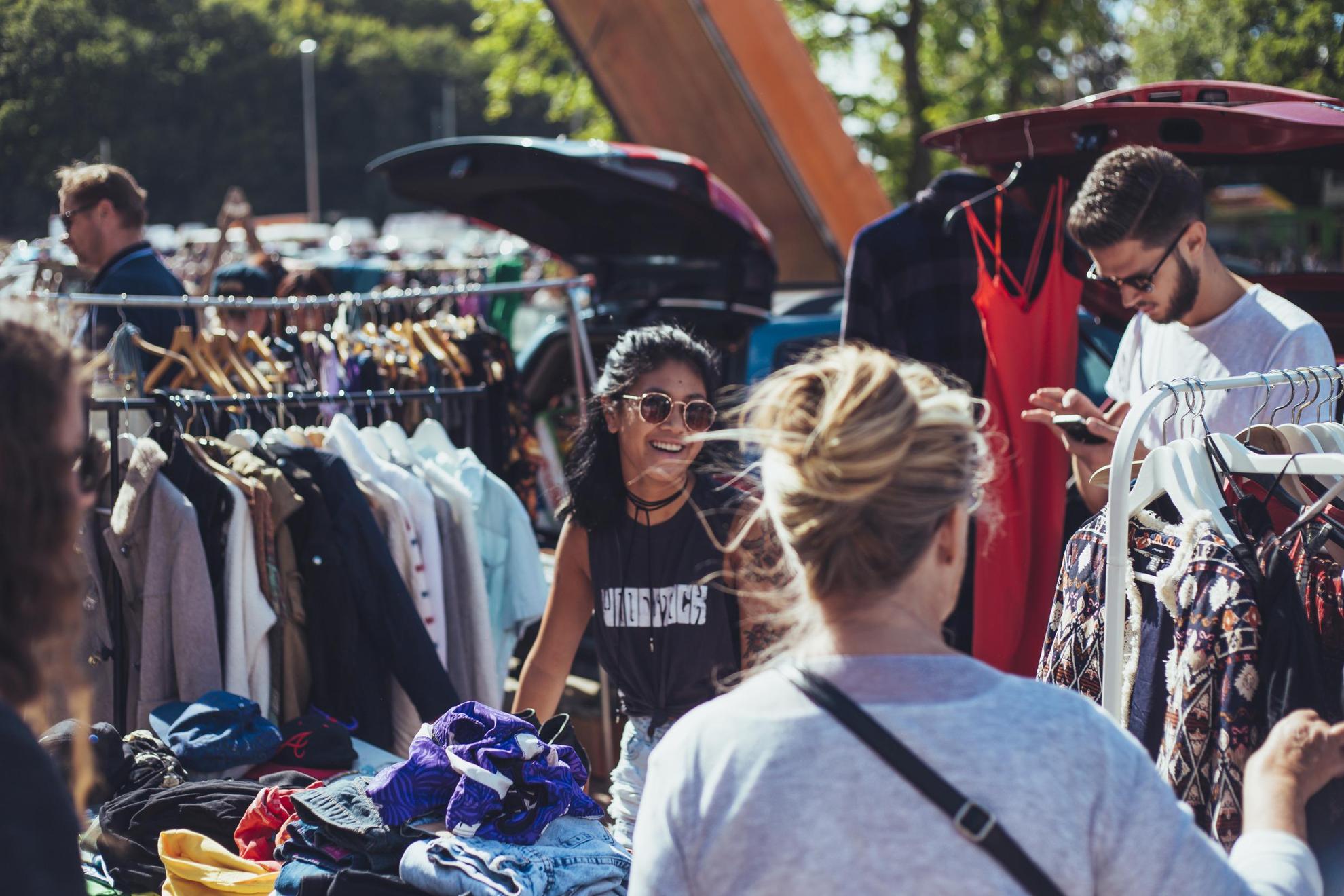 Shoppers are perusing clothes at an outdoors flea market.