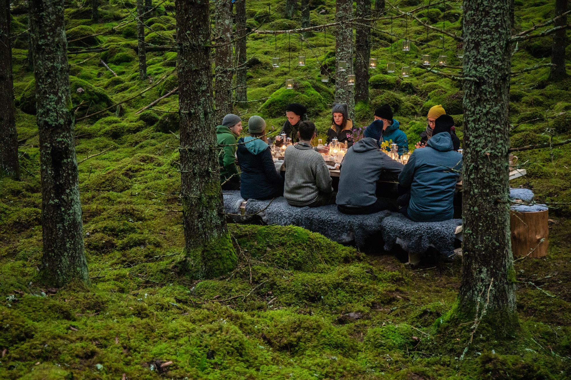 A group of people sitting at a wooden table in the forest.