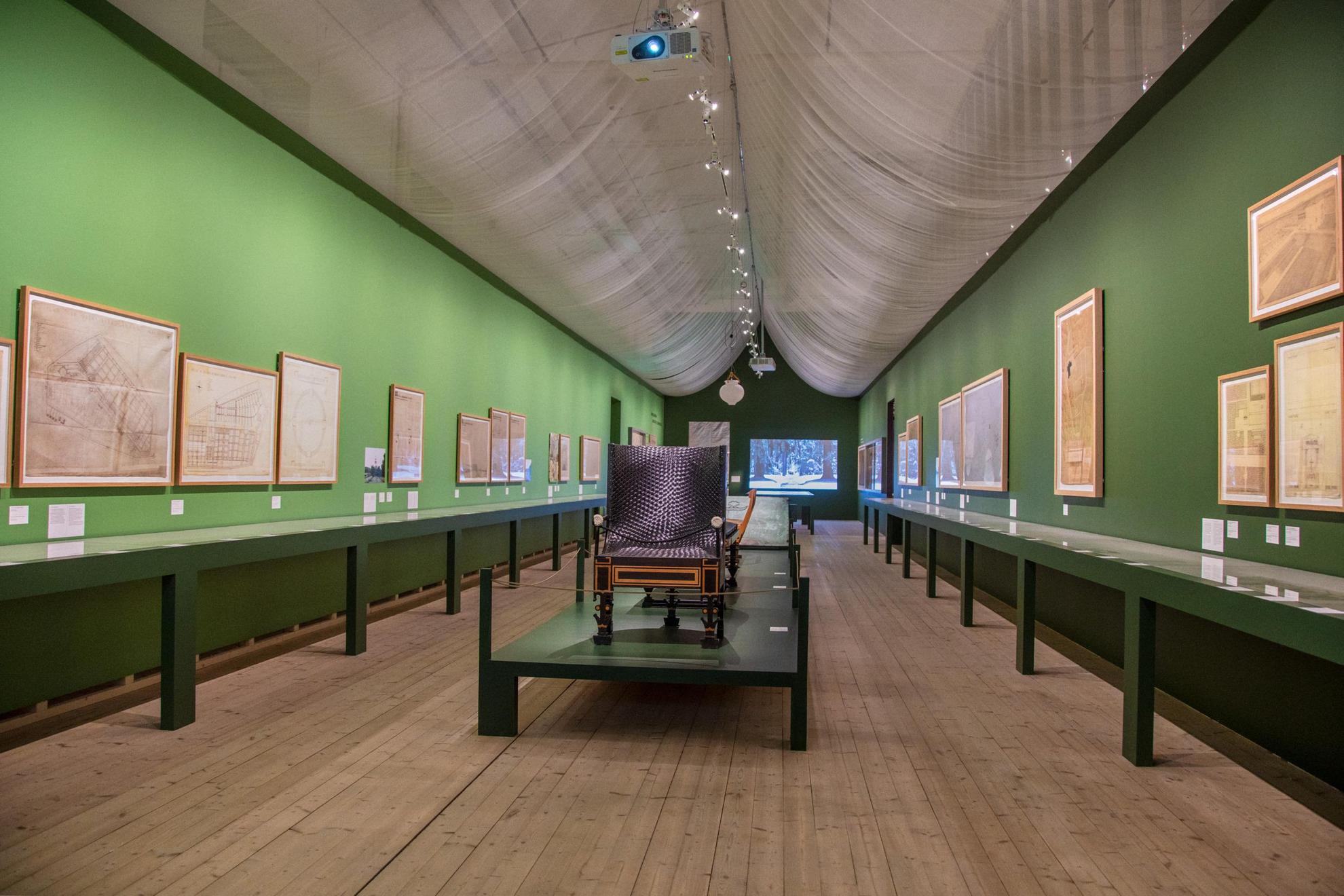 Une exposition d'art avec des peintures sur les murs verts et du mobilier au milieu de la salle.