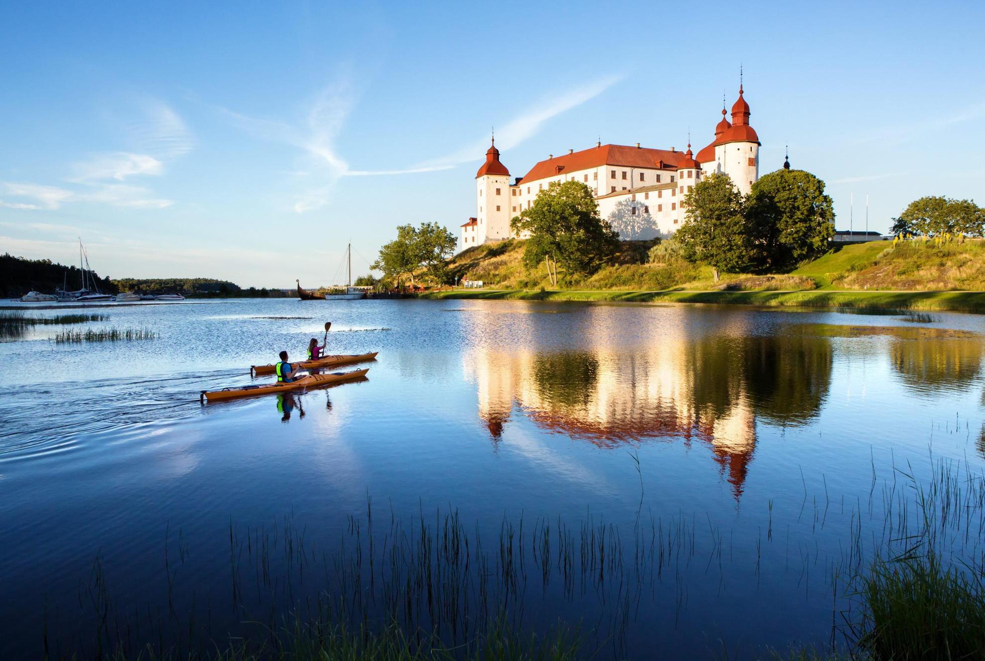 Deux personnes font du kayak sur un lac  en été à côté d'un grand château blanc.
