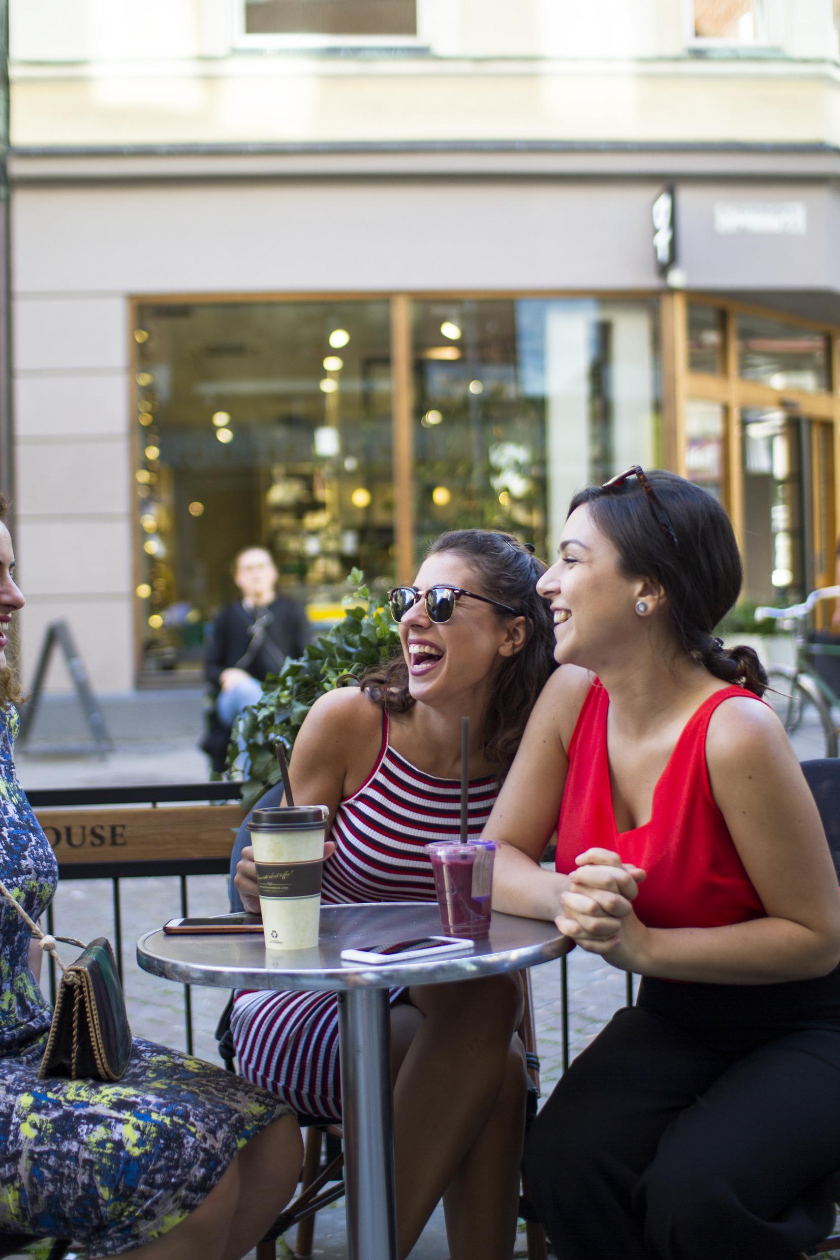 Trois femmes assises en extérieur à Malmö prenant un café et d'autres boissons et souriant et riant.