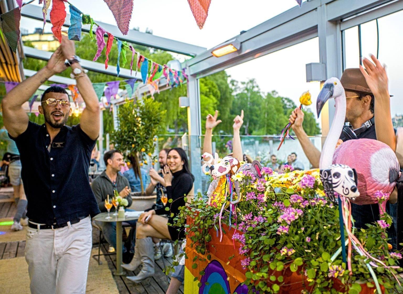 Des personnes profitent d'un moment festif à Mälarpaviljongen, avec un décor coloré et un flamant rose au premier plan.