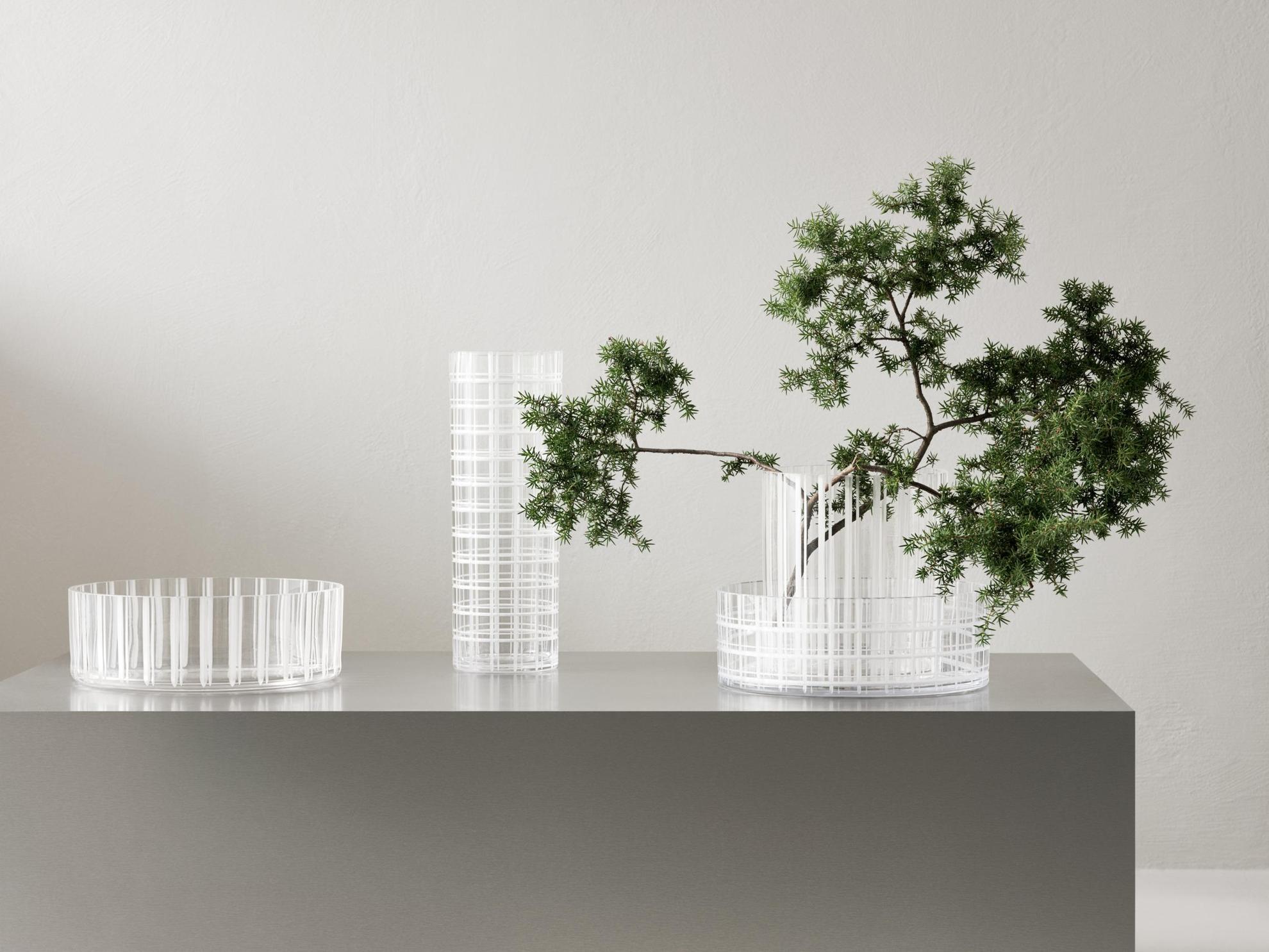 Quatre vases transparents à rayures sur un meuble gris. L'un des vases contient une petite branche d'arbre.