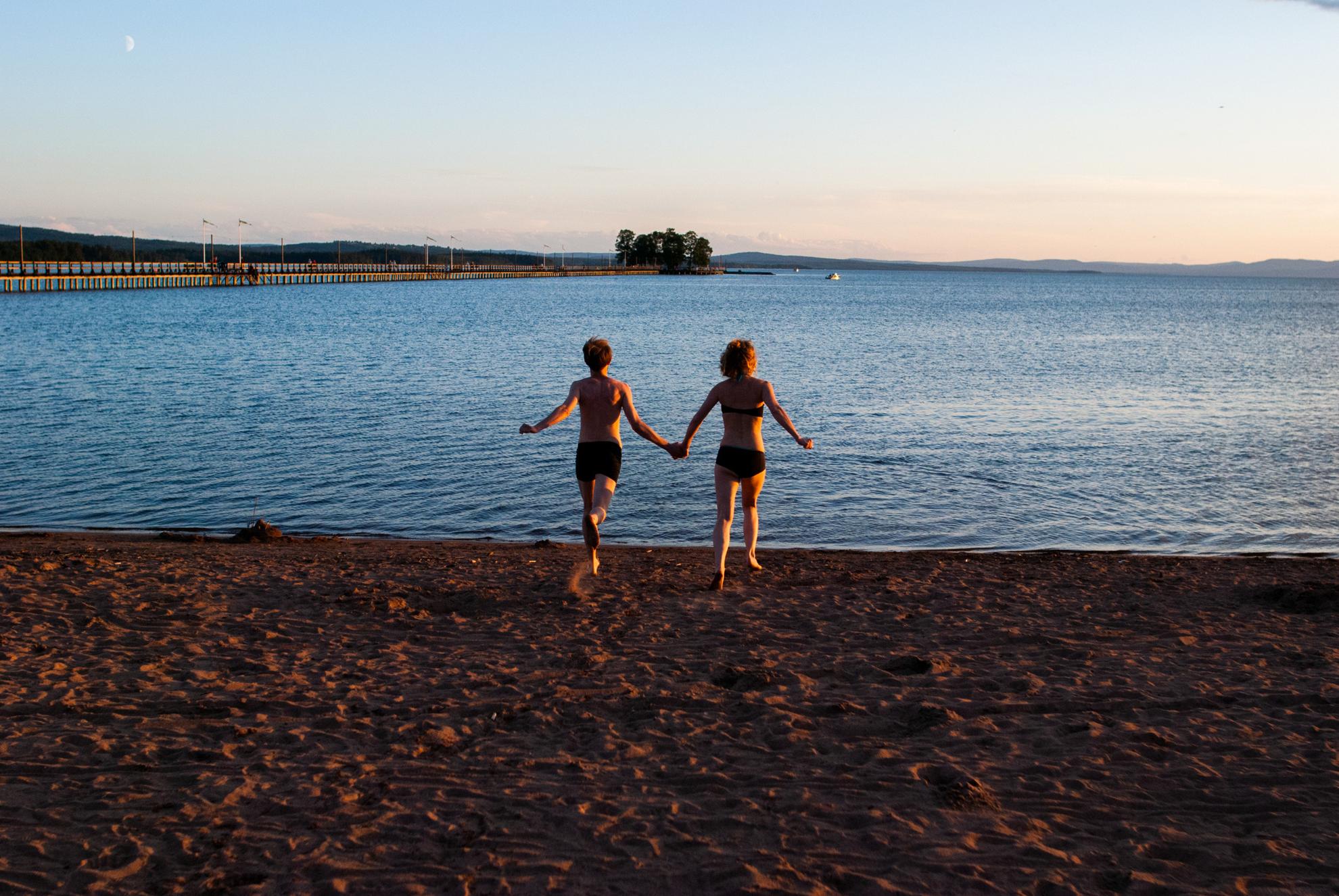 Deux personnes en maillot de bain courant sur une plage en direction de l'eau.