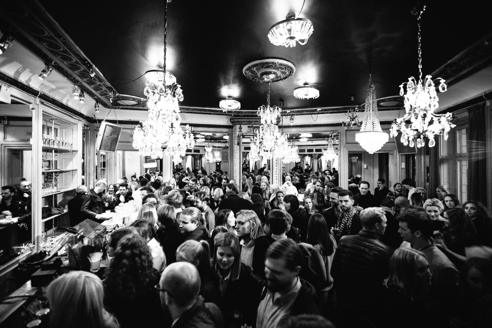 Une photo en noir et blanc d'une foule chez Spy Bar à Stockholm. Des chandeliers sont suspendus au plafond.