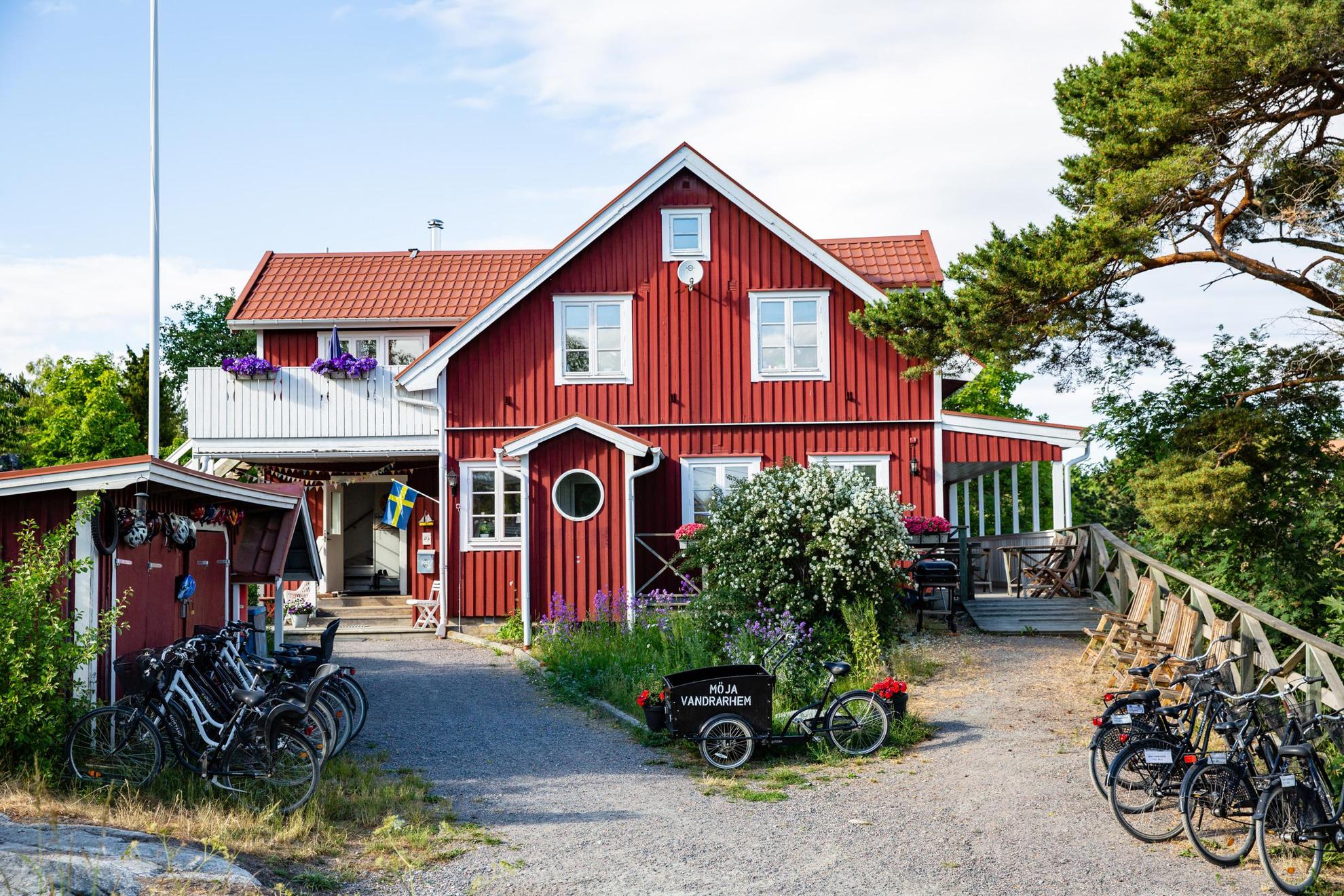 Une maison en bois rouge avec des bordures blanches en été. Il y a plusieurs vélos à l'extérieur de la maison. Sur l'un des vélos, il est écrit "Möja Vandrarhem".