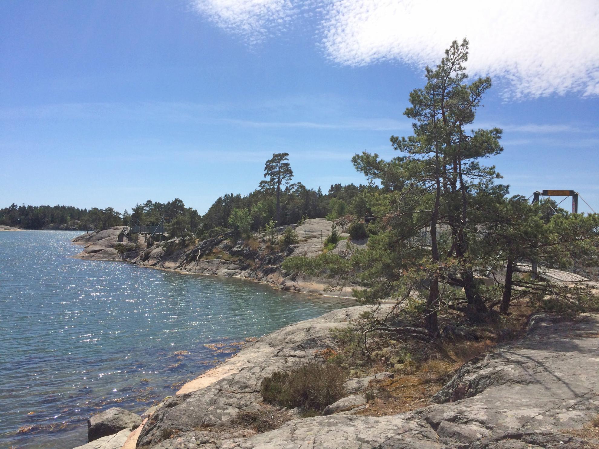 Des arbres poussent sur les rochers, l'eau se trouve sur le côté gauche. Derrière les arbres, on reconnaît à peine les petits ponts qui relient les îles rocheuses.