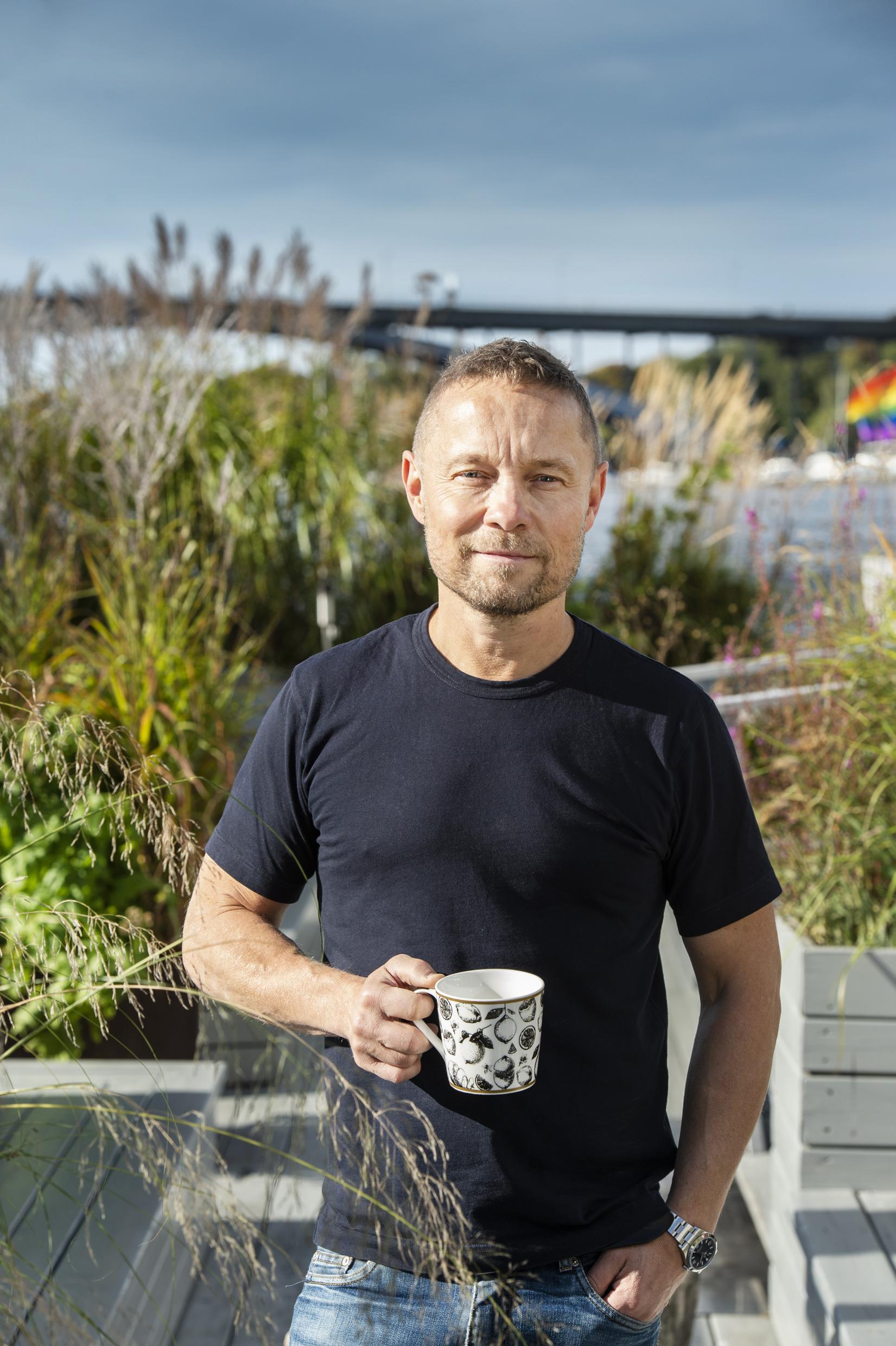 Arto Winter debout devant des espaces de verdure avec une tasse de café à la main