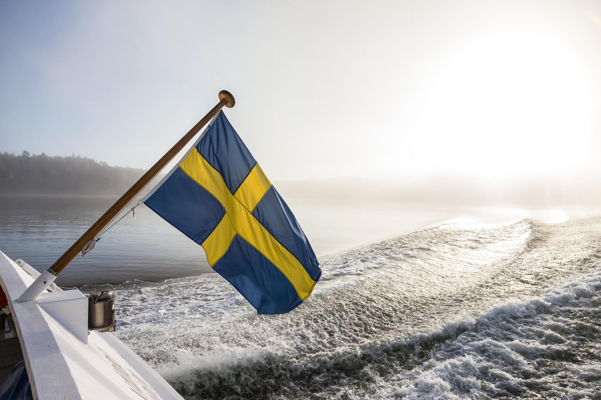 Un drapeau suédois flotte au vent à l'arrière d'un bateau à moteur.