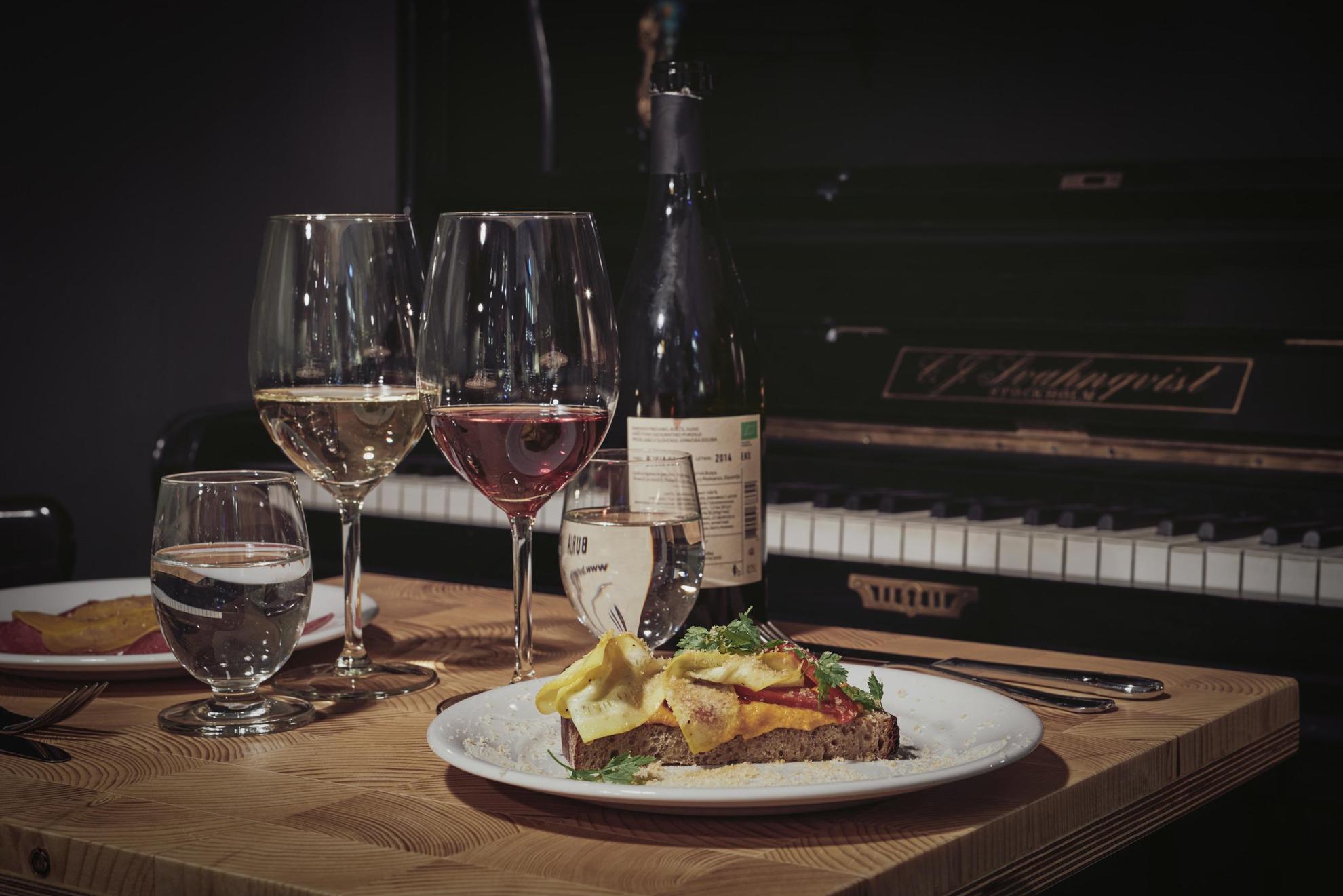 Une table dressée avec une bouteille de vin, deux assiettes de nourriture et deux verres de vin. La table se trouve à côté d'un piano.