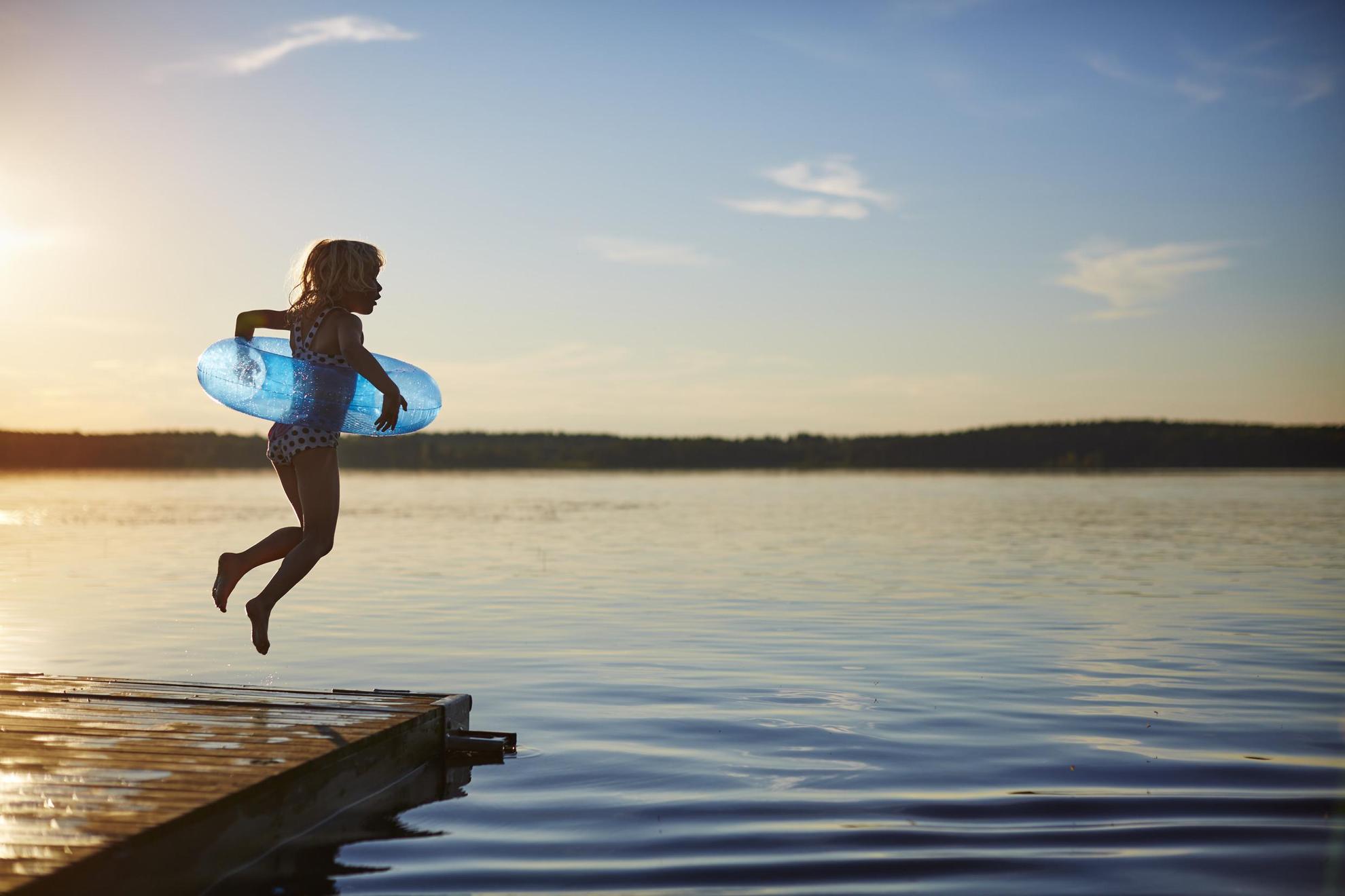 A girl with an inflatable swim ring is jumping into the lake from a wooden pier.