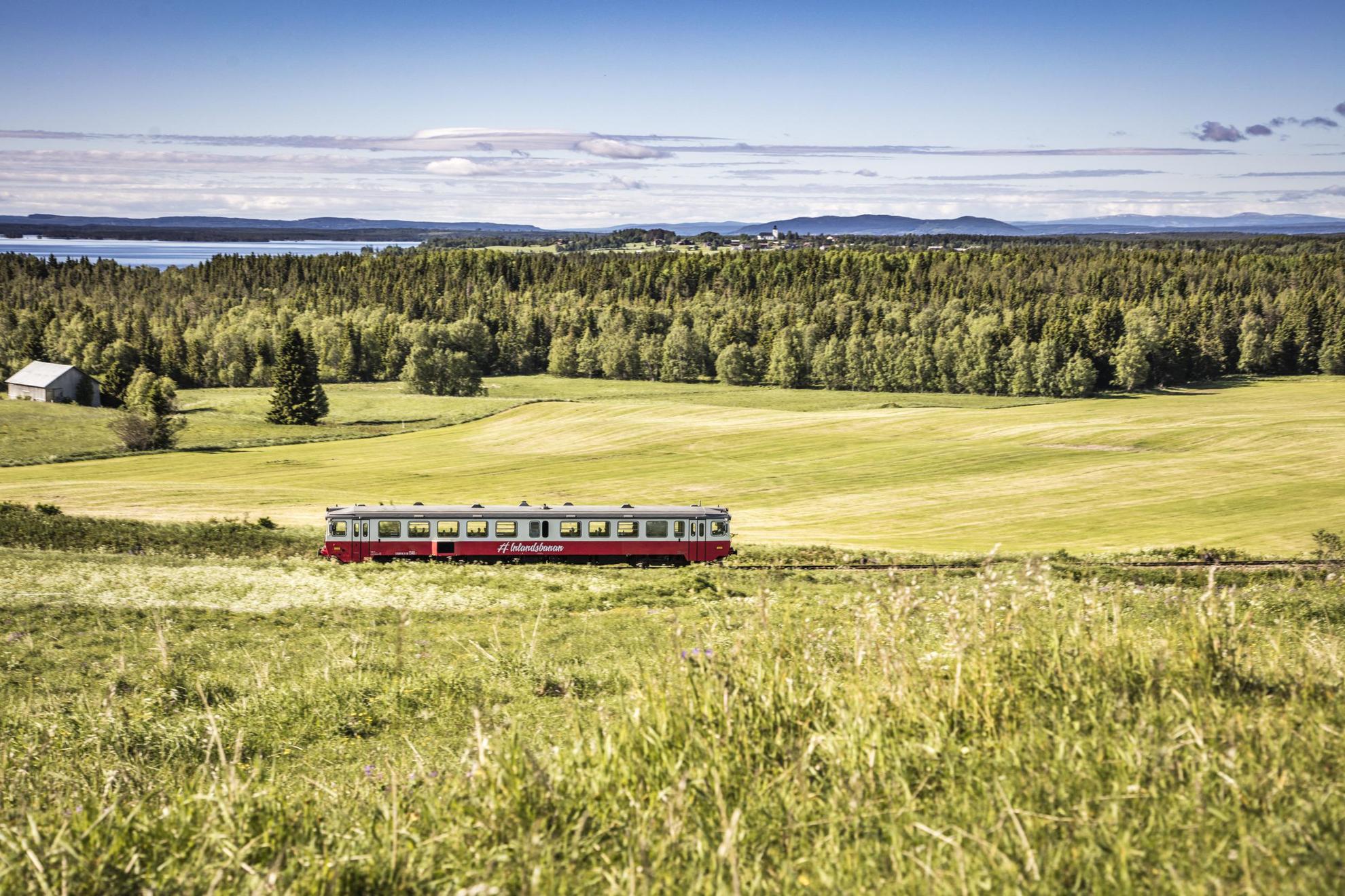 Un train traversant des champs avec au loin des forêts, de l'eau et des montagnes.