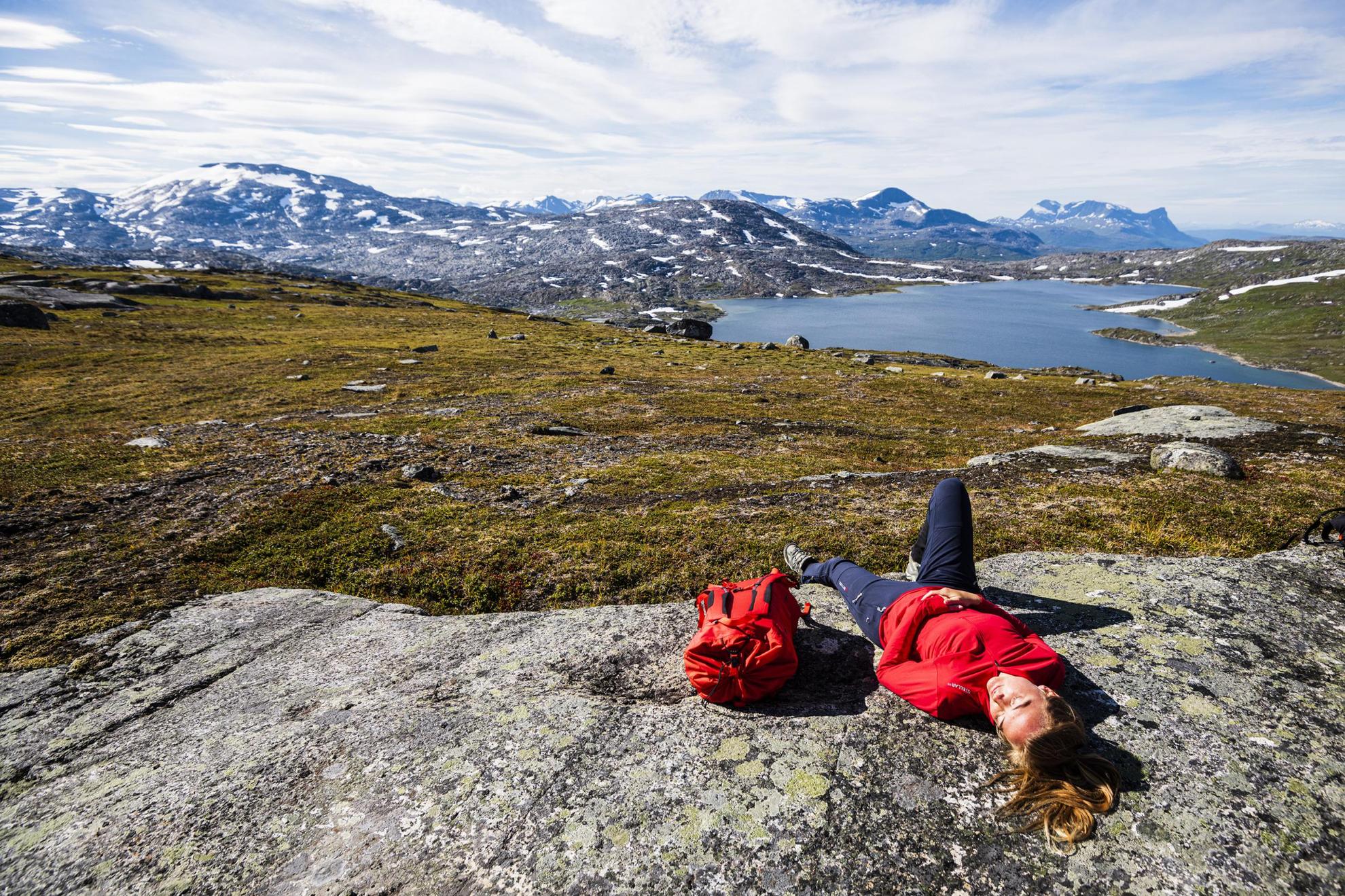 Une femme se repose, allongée sur un rocher. En arrière-plan, on voit les montagnes d'Abisko et un lac.