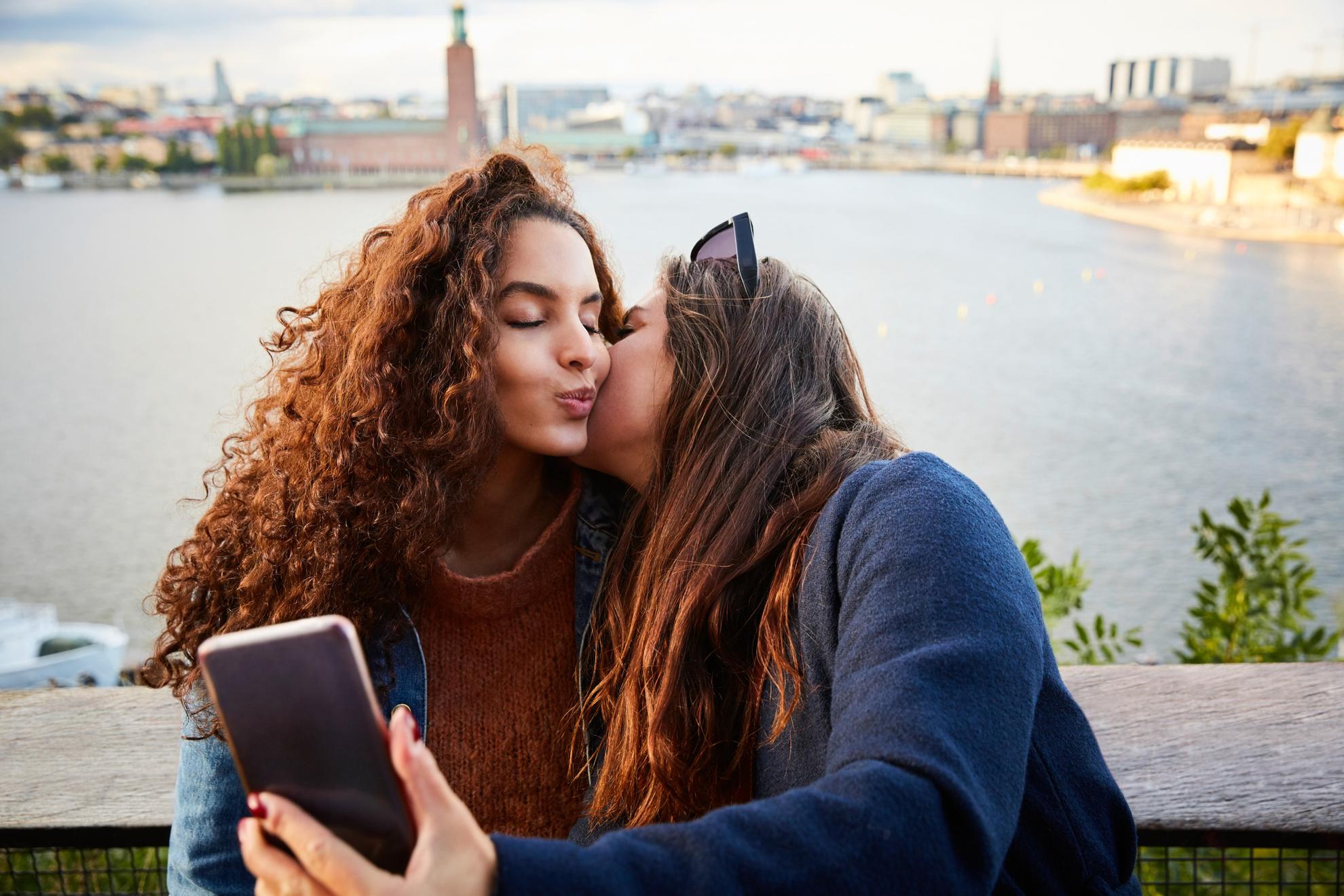 Deux femmes se tiennent sur un pont et prennent un selfie en s'embrassant.