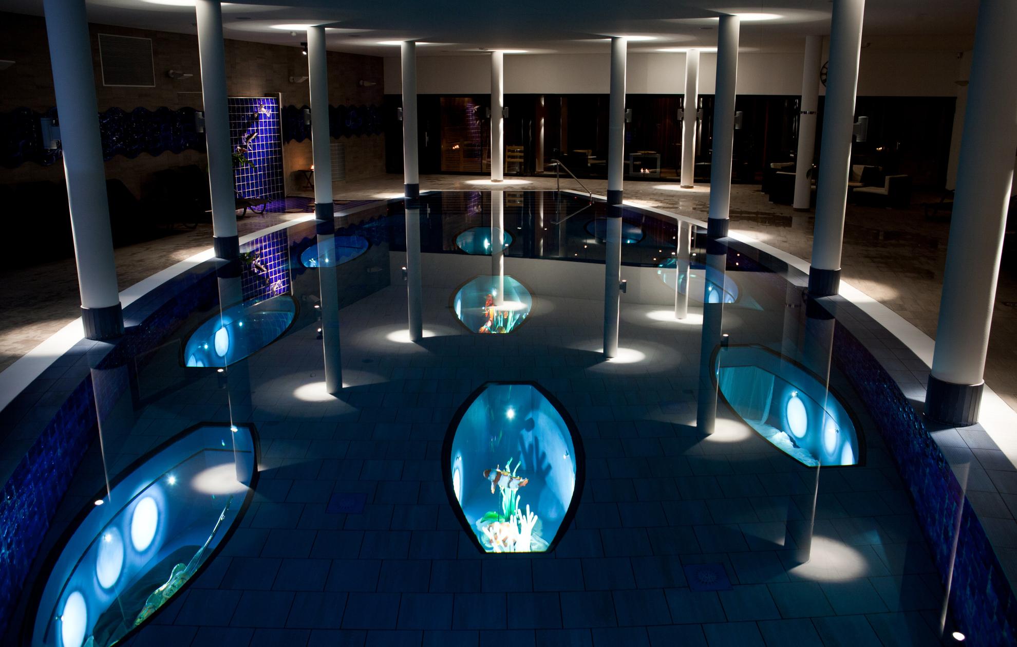 Une piscine intérieure dont la lumière est tamisée. Dans la piscine se trouvent des expositions d'art illuminées avec des poissons en verre.