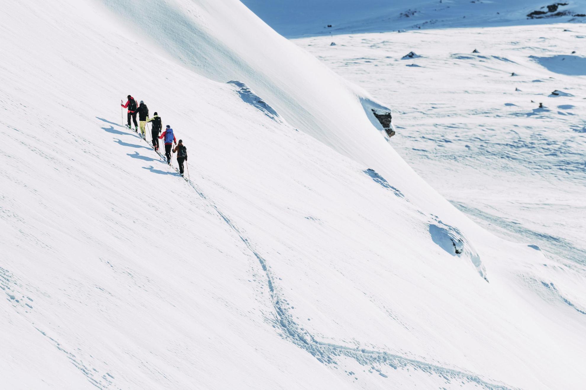 Cinq personnes à skis gravissent une montagne enneigée.