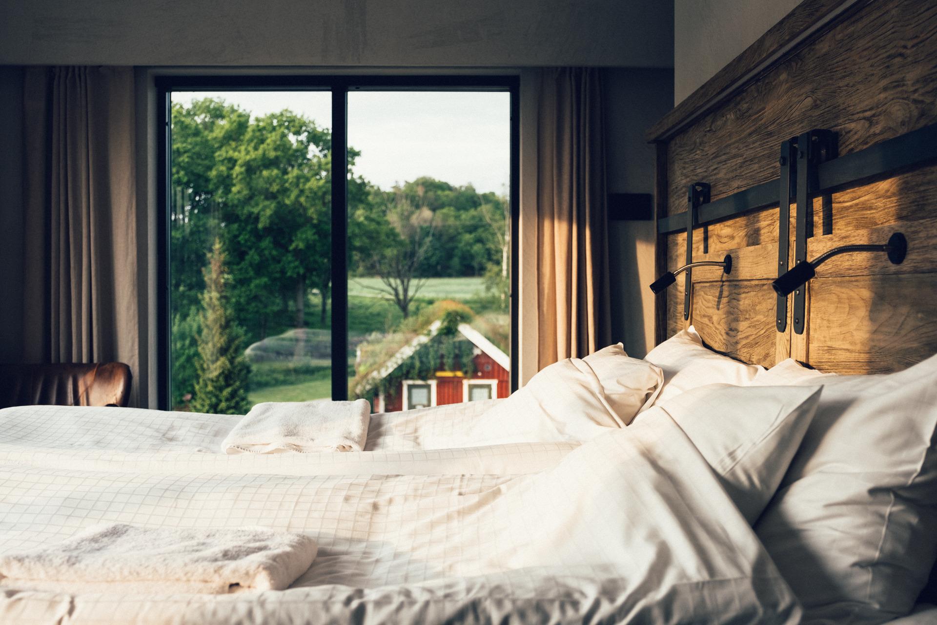 Un lit double dans une chambre d'hôtel dont les fenêtres donnent sur une cabane rouge et une forêt.