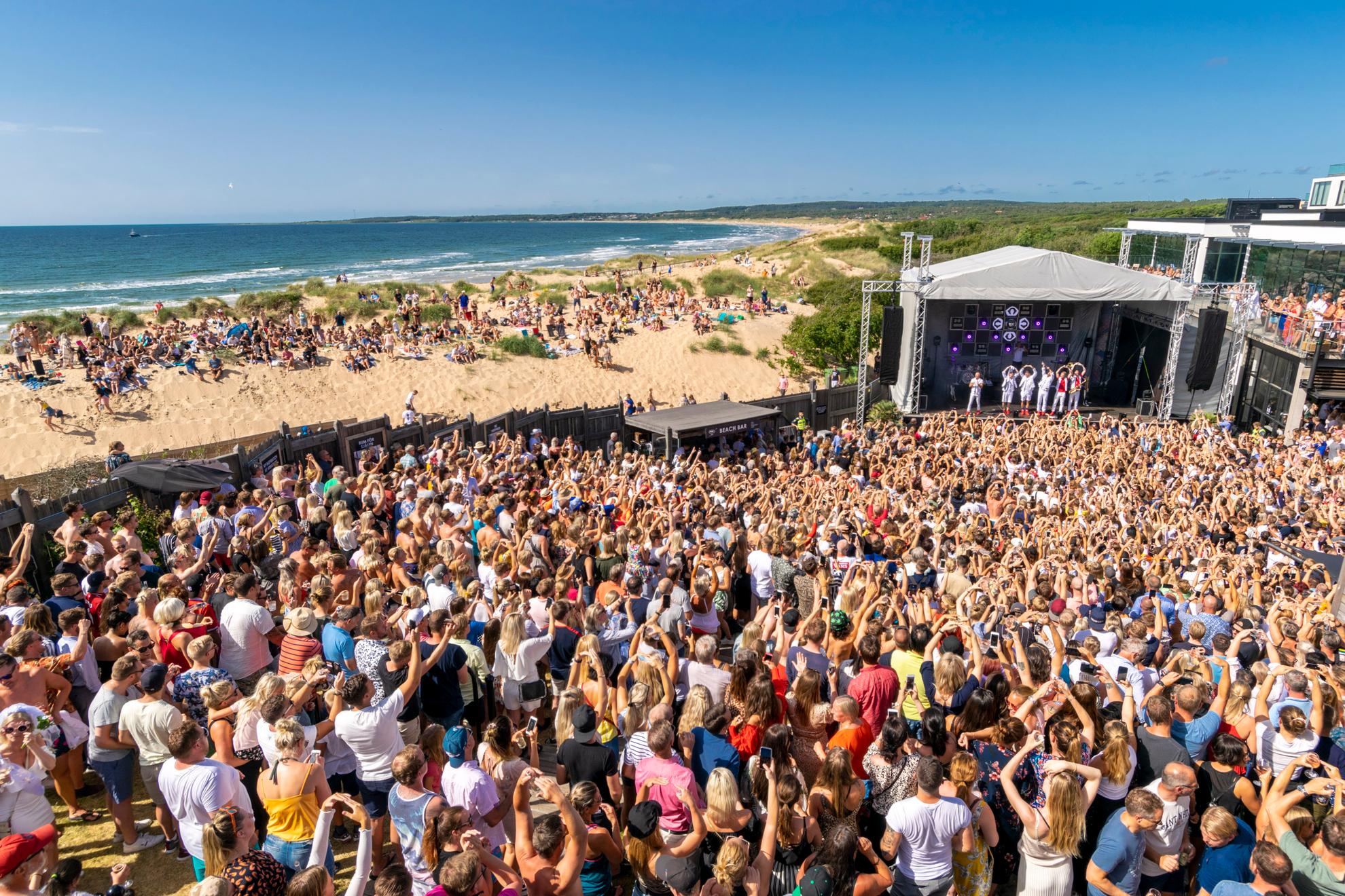 Une grande foule se tient devant une scène sur la plage à côté de la mer.