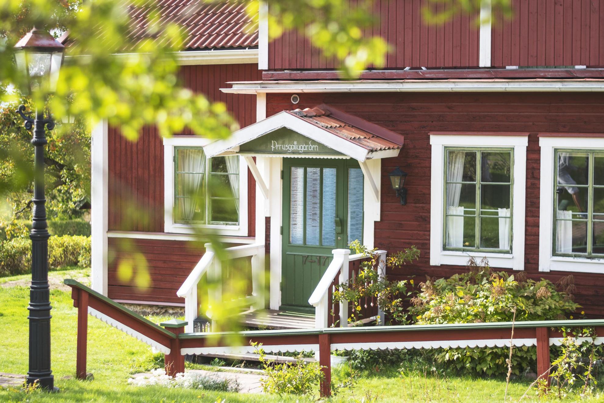 Une maison en bois rouge avec des encadrements blancs et une porte verte.