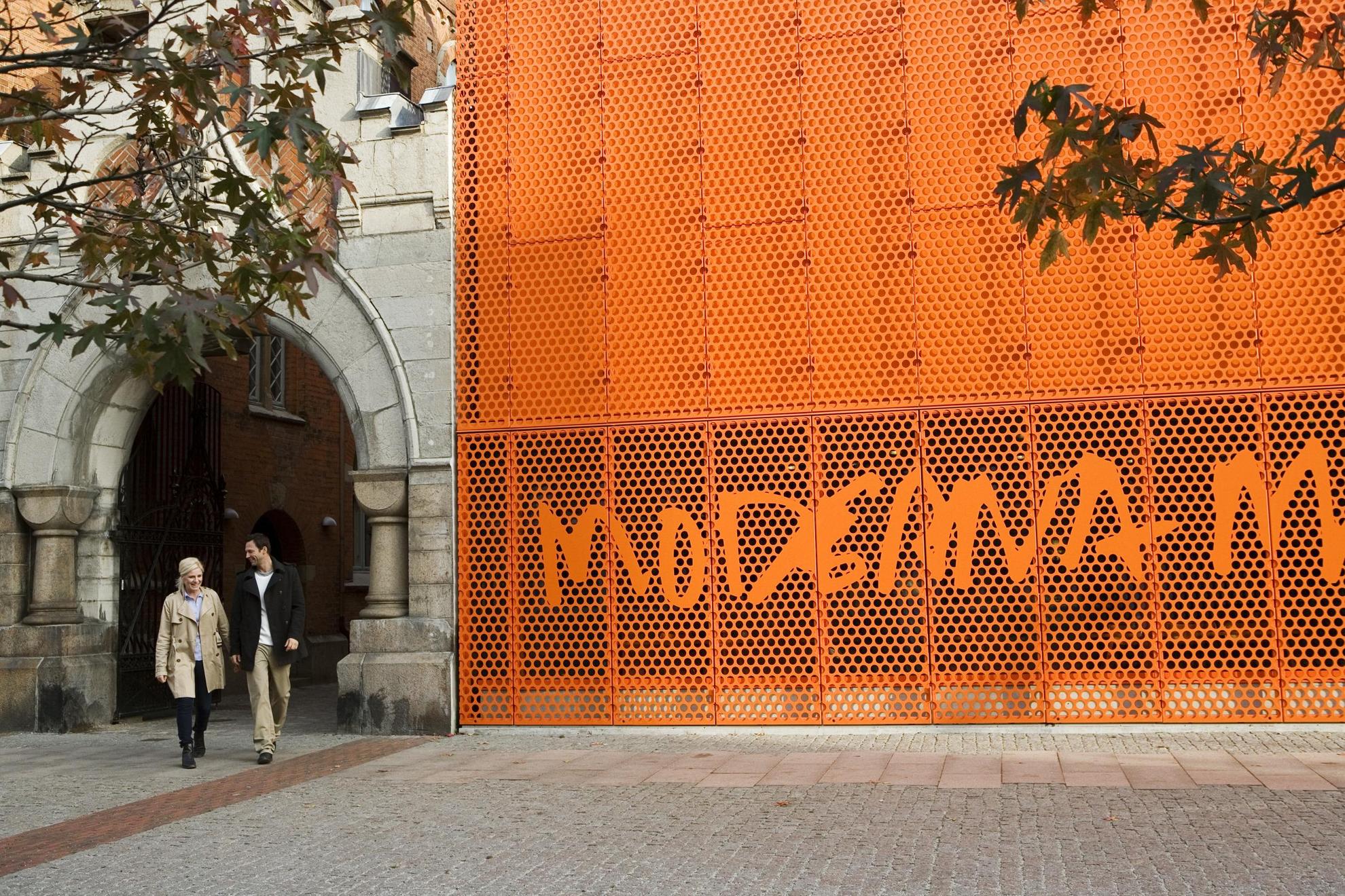 Un homme et une femme passent devant l'enseigne orange du Moderna Museet à Malmö.